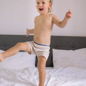 A cheerful child enjoying a playful moment jumping on a bed in a cozy bedroom setting.